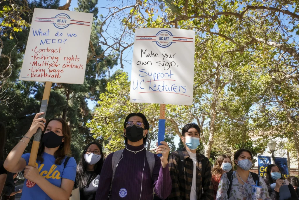 UCLA students carry pickets reading "Make Your Own Sign. Support UC Lecturers" and "What do we Need? Contract, Rehiring Rights, Living Wage, Health Care" at a UC-AFT rally.