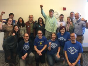 Members of the Unit 18 bargaining team, several wearing blue UC-AFT T-shirts, others raising their fists, at UC Davis in 2019.