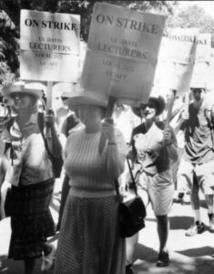 Black and white image shows a march of faculty, staff, and students at UC Davis during UC-AFT's strike in 2003. The woman featured in this image are carrying pickets that read "On Strike - UC Davis Lecturers - Local 2023 UC-AFT"