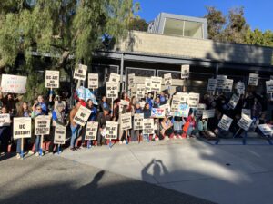 Demonstration teachers and their students and supporters outside the UCLA Lab School entrance during their strike in 2023. They are holding picket signs reading "UC Unfair!" "UC-AFT On Strike" "Refusal to bargain is bad faith" and "Unfair Labor Practice Strike!"