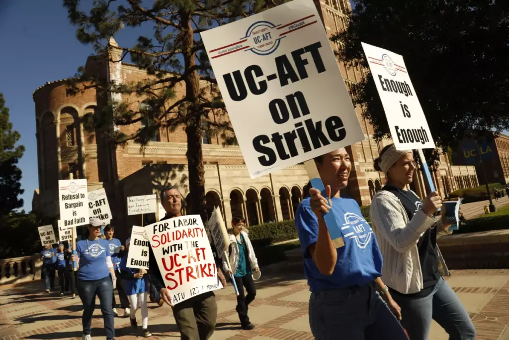 Demonstration teachers marching outside Royce Hall carrying picket signs during the Lab School Strike at UCLA in 2022. Their signs read "UC-AFT on Strike." "Enough is Enough" "For Labor Solidarity with the UC-AFT Strike! ATU 1277 Member" and "Refusal to Bargain is Bad Faith"