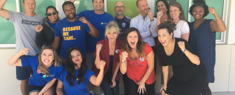 A group of teachers outside the Preuss School smiling with their fists raised.