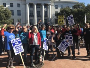 Lecturers and librarians supporting their UAW colleagues during their strike in 2022. Several are raising their fists and holding picket signs reading "UAW On Strike - Unfair Labor Practice" and "Academic Workers United"