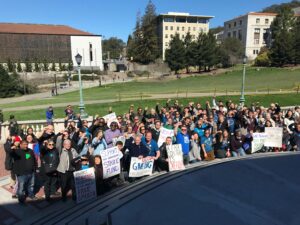 Librarians and their supporters, many raising their fists, gather on the quad at UC Berkeley in 2018. Several carry home made signs reading "Protect Academic Freedom at the home of Free Speech," "Support the librarian strike fund", "A Fair Contract is Overdue" and "Librarians Working = Student Learning"