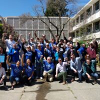 Members of the UC-AFT bargaining team and supporters raising their fists and wearing blue t-shirts outside of a bargaining session in April 2019 at UC Davis.