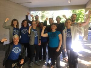 Lecturers at UC Davis smiling and raising their fists in blue UC-AFT t-shirts in 2019. In the background is CFT President Jeff Freitas.