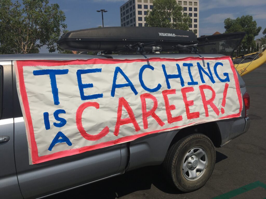 A banner fixed to a truck with a kayak sticking out of the back reads "Teaching is a Career!"