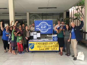 Members of the Unit 18 Bargaining team gather outside Charles Young Library during a bargaining session in 2019. They raise fists and stand near a table with UC-AFT banners.