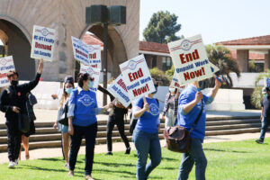 Members of UC-AFT, many in masks and blue union t-shirts, marching with students and carrying picket signs reading "End Unpaid Work Now!" and "UC-AFT Faculty Demand Job Security" at UCSB in 2020.