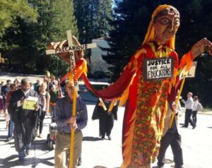 Members of UC-AFT photographed while participating in a National Adjunct Walkout Day at UC Santa Cruz in 2015. They are wearing all black and carrying large handmade masks as well as a large puppet called “Saint Precariat” adorned with a sign that reads "Justice for All Educators".