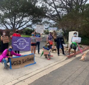 UC-AFT members wearing masks and costumes and holding signs during a car caravan action at UC San Diego in 2020. Their handmade signs read "Higher Ed Not Uber Ed", "UCSD Lecturers," "Fair Contract Now" and "UCSD Lecturers Need a Fair Contract Now!"