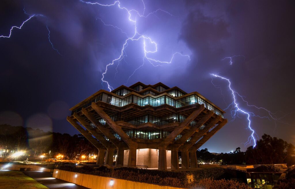 The Geisel Library at UCSD at night. A lighting bolt breaks in the sky just above it, giving the image a purplish hue.