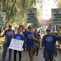 Lecturers in blue union t-shirts carrying green and white picket signs reading "On strike for Unfair Labor practice - AFSCME 3299"