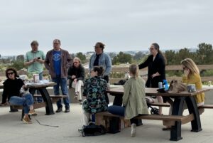 folks gathered around two picnic tables on a balcony listening to a speaker (not pictured)