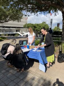 two women at a table having out flyers. Two other women crouch in front of the table, their backs to the camera