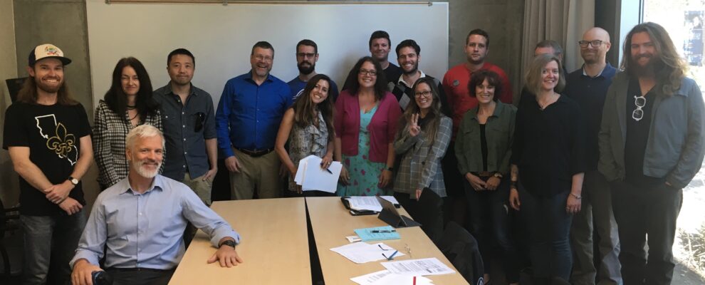 a group of 16 people pose smiling in a conference room.