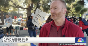 A bearded man wearing red is interviewed by the local NBC news affiliate